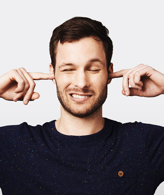 Mann mit Zeigefingern in den Ohren links und rechts und verzehrtem Gesicht